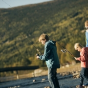 Tre personer som fisker med fiskestang ved elvebredden.