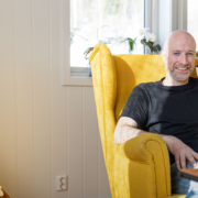 Portrettbilde av Sveinung Dahl, i en gul stol og en kaffekopp i hånda.